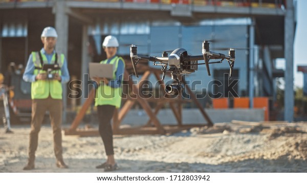 Diverse Team of Specialists Pilot Drone on\
Construction Site. Architectural Engineer and Safety Engineering\
Inspector Fly Drone on Commercial Building Construction Site\
Controlling Design and\
Quality