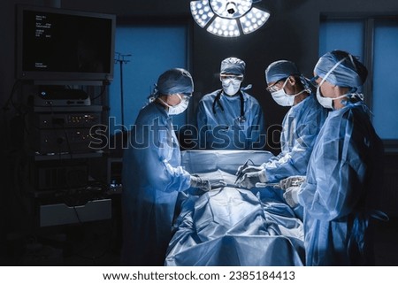 Diverse team of surgeons performing surgery on patient in hospital operating room. Urgent treatment, plastic surgery. Specialists saving patient`s life in operation theater.