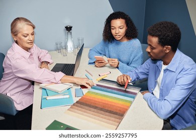 Diverse team of three designers choosing color of upholstery on fabric samples while creating interior design collaboratively sitting at table at workplace - Powered by Shutterstock