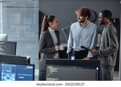 Diverse team of three young people standing in formal office setting with multiple computers and chatting copy space - Powered by Shutterstock