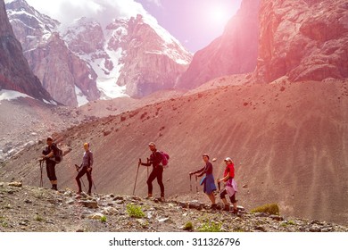 Diverse Team Walking On Rocky Ridge.
Grassy Ridge And Group Of People Walking With Hiking Gear Severe High Mountain Landscape Background Blue Sky White Clouds Shining Sun