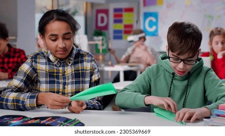 Diverse teen students do origami in classroom at school. Multiethnic schoolgirl and schoolboy having workshop class making paper plane - Powered by Shutterstock