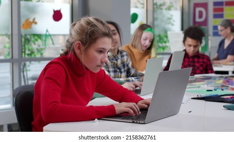 Diverse Teen Students Type On Laptop Sitting At Desk In Classroom. Kids Working On Computer In Modern Class