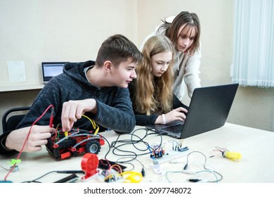 Diverse teenager pupils build robot vehicle learning at table at STEM. Classroom with pupils learning programming language and software design using laptop compute