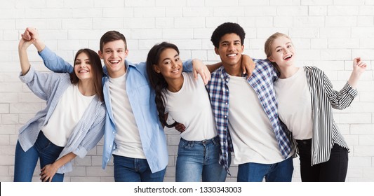 Diverse teenagers embracing and having fun over white brick wall