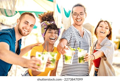 Diverse trendy friends having fun drinking mojito cocktails at sunset beach party - Summer joy and life style concept with fancy people at chiringuito happy hour - Warm filter with focus on left woman - Powered by Shutterstock