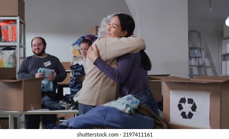 Diverse volunteers smile and hug working in non-profit organization. Group of activists sort and pack second-hand clothes for recycling in military warehouse - Powered by Shutterstock