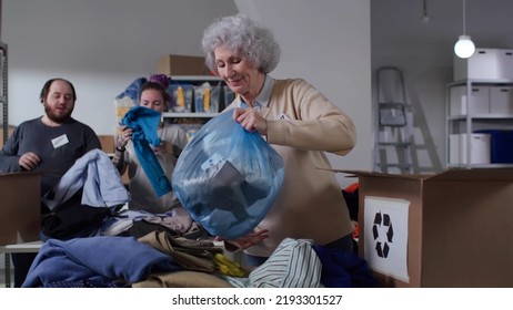 Diverse Volunteers Sort Donated Clothes For Recycling In Eco-friendly Community. Group Of Activists Work In Sorting Warehouse In Recycling Center