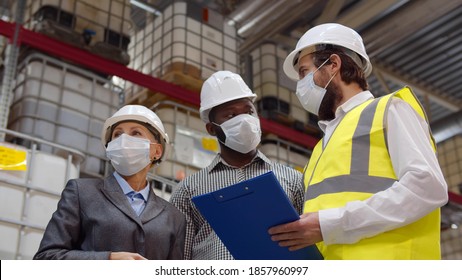 Diverse Warehouse Inspectors Wearing Safety Mask Discussing Distribution Plan On Clipboard. Industrial Warehouse Engineer, Manager And Owner In Protective Mask Inspecting Distribution Center