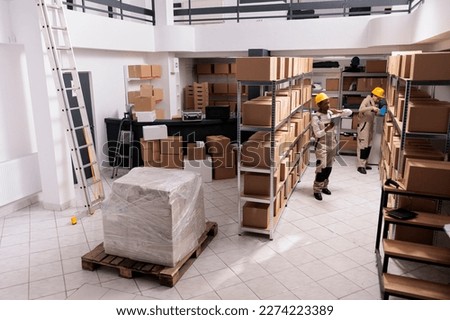 Diverse warehouse workers packing packages and checking parcels in stockroom. Delivery company storehouse employees using adhesive tape on cardboard boxes and searching package on shelf