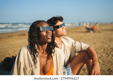Diverse watching solar eclipse on a beach wearing protective glasses