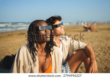 Diverse watching solar eclipse on a beach wearing protective glasses