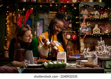 Diverse women couple making Christmas cookies and icing gingerbread house in decorated kitchen on New Year's eve - Powered by Shutterstock