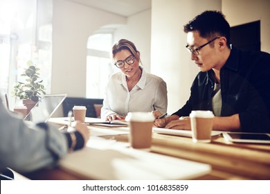 Verschiedene Arbeitskollegen lächeln und diskutieren ein Projekt, während sie an einem Tisch in einem modernen Büro sitzen 