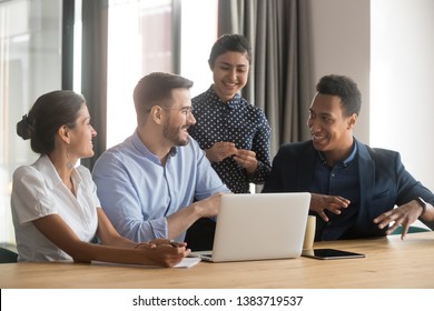 Diverse Work Team Sit At Office Desk Talking Brainstorming On Project Strategy, Smiling Multiethnic Employees Discuss Share Ideas Cooperating Using Laptop At Office Meeting. Collaboration Concept