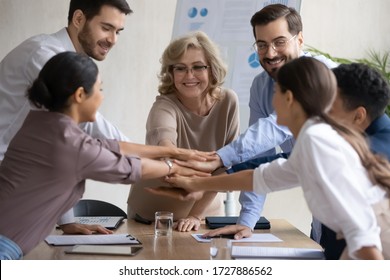 Diverse workers with mature mentor, putting hands together, showing support and unity after successful presentation at company meeting. Happy female teacher with colleagues in team building activity.