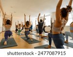 Diverse yoga class executes a kneeling arm stretch, enhancing balance and flexibility in a serene, sunlit studio with wooden flooring