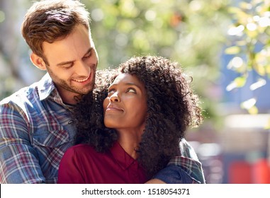 Diverse young couple lovingly looking into each other's eyes while standing together outside on a sunny day - Powered by Shutterstock