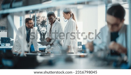 Diverse Young Group of Engineers Working in a Modern Startup Lab. Male Specialist Soldering a Circuit Board While Team of Professionals Discuss Technological Project Strategy Using Laptop Computer.