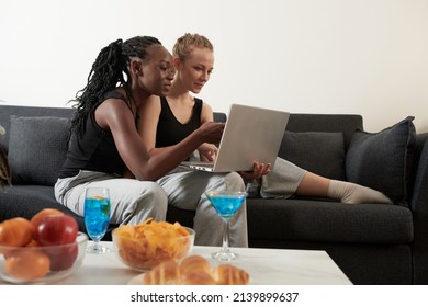 Diverse Young Lesbian Couple Having Drinks And Snacks When Shopping Online