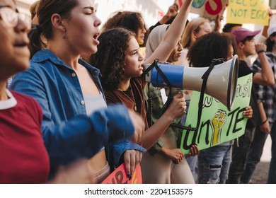 Diverse young people marching for climate justice with banners and a megaphone. Group of multicultural youth activists protesting against global warming and climate change in the city. - Powered by Shutterstock