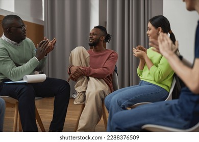 Diverse young people in support group circle applauding to smiling black man sharing success story - Powered by Shutterstock