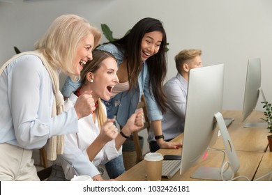 Diverse young and senior female colleagues excited by online win or business achievement, multiracial happy businesswomen celebrating victory looking at computer screen watching cheering winning team
