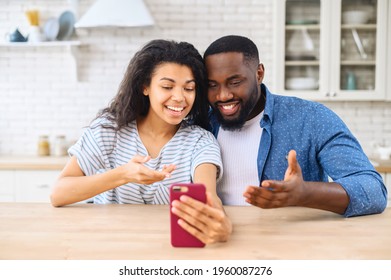 Diverse Young Spouses Talking Via Video Call, Involved Into Video Meeting, Webinar On The Smartphone, Happy Multiracial Couple Using Phone For Video Connect