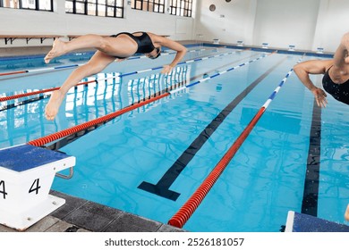 Diverse young swimmers diving into indoor swimming pool, training for meet. A biracial female in black swimsuit and a Caucasian male showing strength and focus, unaltered - Powered by Shutterstock