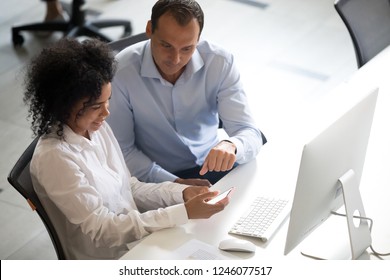 Diversity colleagues using smartphone together at workplace, checking social network, African American woman holding phone in hands, using mobile apps, black intern taking mentor phone number
