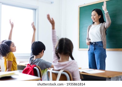 Diversity of elementary school students raise their hands to answer teacher questions in class room. Back to school concept