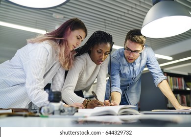 Diversity Group Of Smart Male And Female Students Collaborating In Library On Writing Coursework For Science Presentation. Intelligent Young Hipster Guys Cooperating During Literature Brainstorming