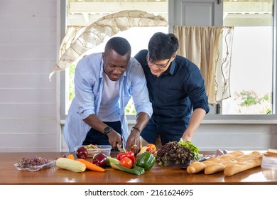 Diversity Of LGBTQ Gay Couple Between Asian And African Ethnicity Cooking Together At Home Using Organic Vegetable To Make Salad And Sandwich