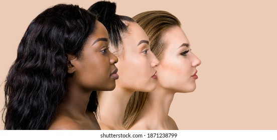 Diversity, Multi-ethnic Beauty Concept. Three Beautiful Ladies Of Different Races, African, Asian And Caucasian, With Natural Makeup, Posing On The Beige Studio Background In Profile, Standing In Row