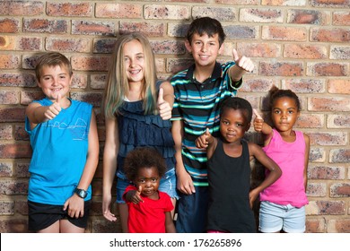 Diversity Portrait Of Kids Against Brick Wall Doing Thumbs Up.