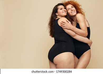 Diversity. Portrait Of Women Of Different Body Types. Hugging Brunette And Redhead In Black Bodysuits Posing On Beige Background. Female Friendship.