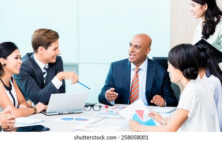 Diversity Team In Business Development Meeting With Charts, Indian CEO And Caucasian Executive Crunching Numbers, Charts And Figures On The Desk