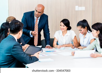 Diversity Team In Business Development Meeting With Charts, Indian CEO And Caucasian Executive Crunching Numbers, Charts And Figures On The Desk