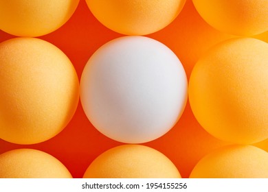Diversity, variation, distinction or contrast concept. White table tennis ball is surrounded by orange ping pong lottery balls. Close up macro view.