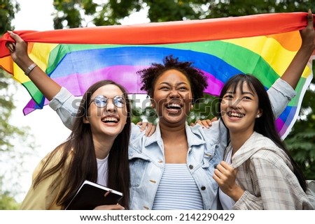 Diversity young gay women with Asian gay waving pride rainbow flag in their backs supporting LGBTQ pride in the park. Independence and polygamy. Supporters of the LGBT community