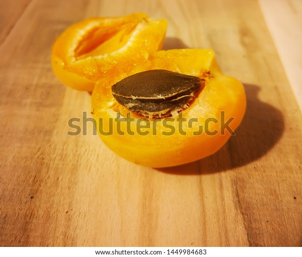 Divided in half apricot lies on a simple wooden\
table in a rustic style. The two halves of the fruit with the\
apricot pit. Hard\
light.