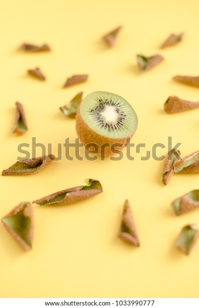 Divided\
in half kiwi among its peel on yellow\
background