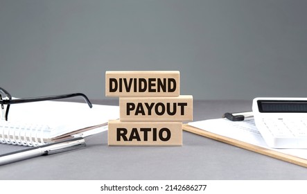 DIVIDEND PAYOUT RATIO text on a wooden block with notebook,chart and calculator, grey background