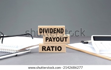 DIVIDEND PAYOUT RATIO text on a wooden block with notebook,chart and calculator, grey background