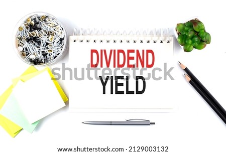DIVIDEND YIELD text on the notebook with office supplies on white background