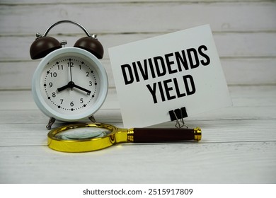 Dividends Yield text on paper card with alarm clock and magnifying glass on wooden background