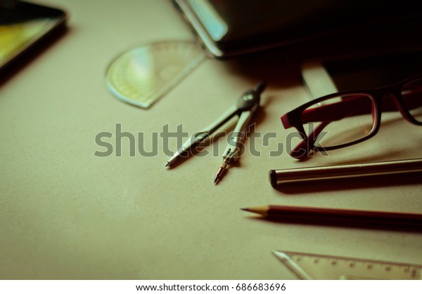 Divider, pencil, pen,\
ruler, glasses and smartphone and blueprint on table top.Table top\
view of Engineers table at office workplace.selective focus.Man\
hand editing\
blueprint.