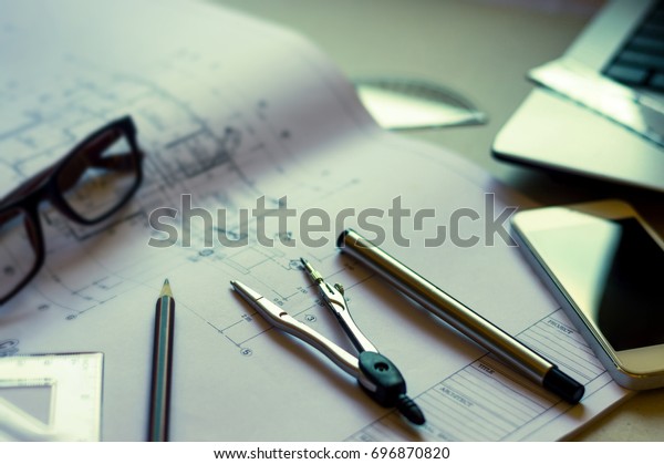 Divider, pencil, pen, ruler, glasses and\
smartphone and blueprint on table top.Table top view of Engineers\
table at office workplace.selective\
focus.
