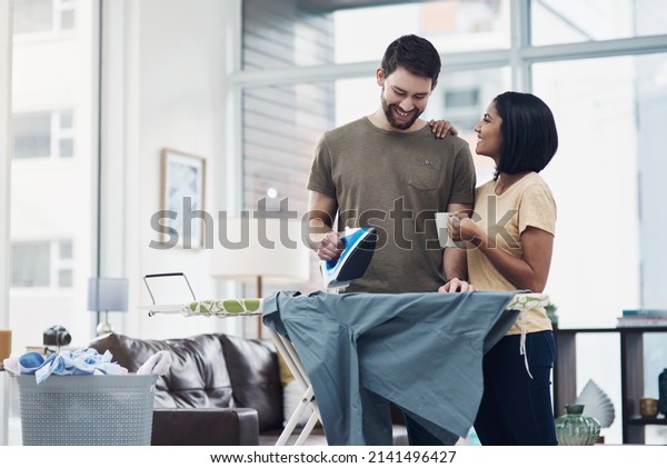Dividing the chores is the simplest way to domestic\
bliss. Shot of a happy young couple ironing freshly washed laundry\
together at home.