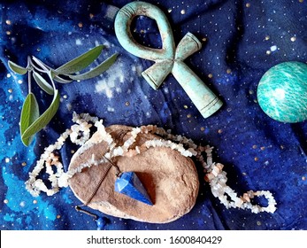 A divination set consisting of moonstone beads, lapis lazuli pendulum, turquoise crytal ball, and Egyptian ankh, and sage on magical blue cloth background